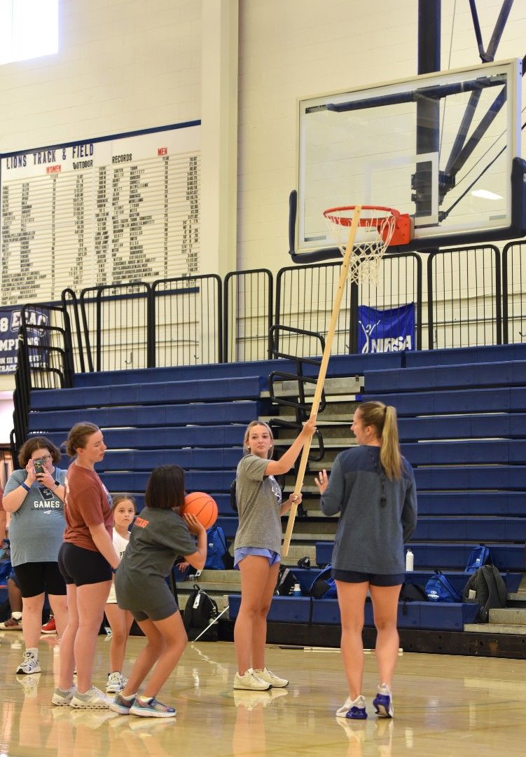 Volunteers use a long pole to tap a basketball hoop for a vision-impaired athlete.