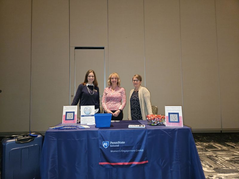 Three women behind a table at a convention