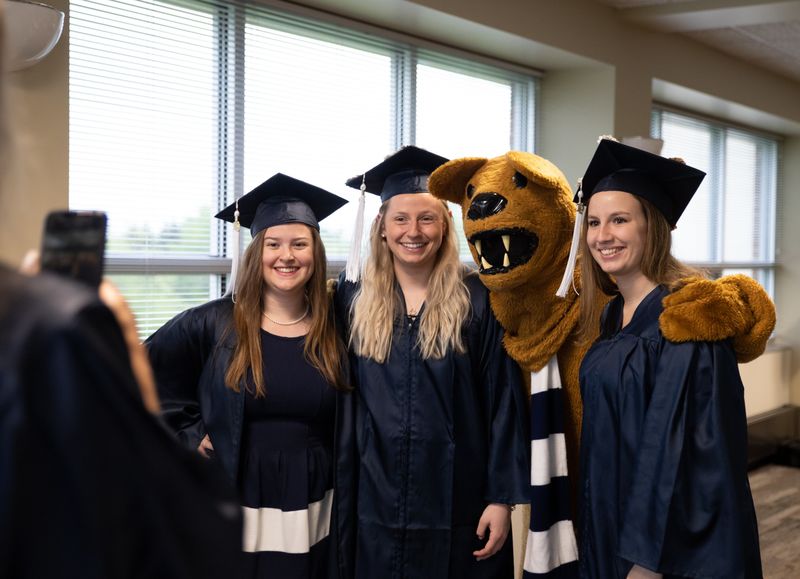 Three female graduates pose with Nittany Lion mascot