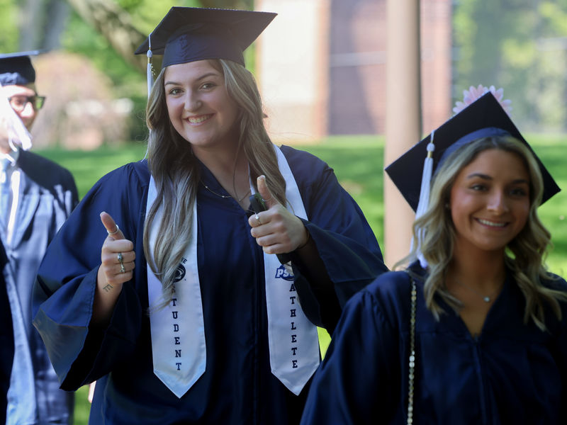 Two women are walking outside wearing commencement caps and gowns.