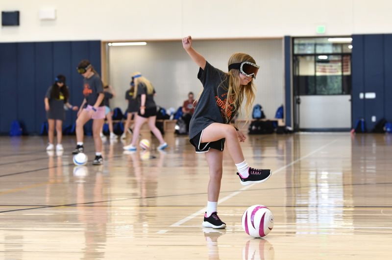 A young athlete wearing blackout goggles kicks a soccer ball.