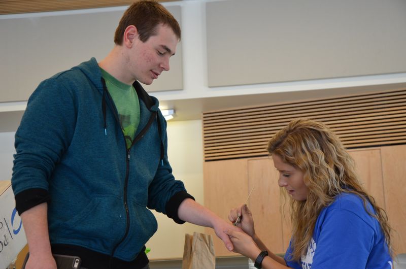 A student painting a green dot on another student's hand