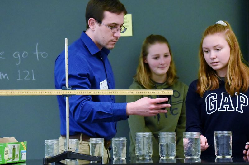 An instructor measures the pitch of a water glass struck by two students in a regional Science Olympiad event.