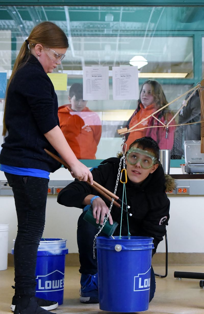 Two students pour sand in a bucket to test the strength of a balsa-wood support.