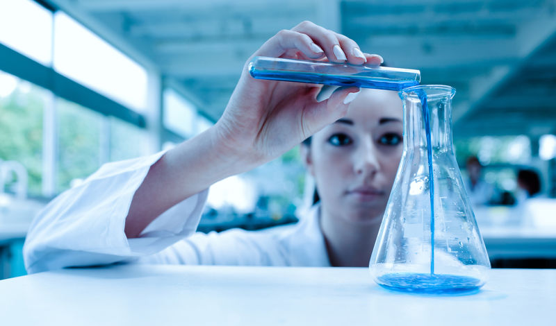 A scientist pours blue liquid into a container.