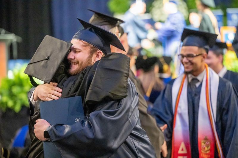 A new graduate hugs a faculty member after leaving the stage at Penn State Behrend's spring 2023 commencement ceremony.