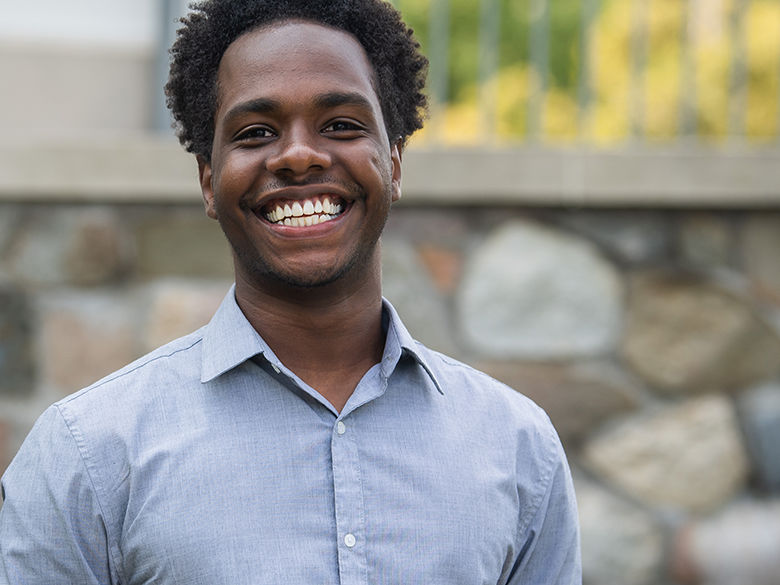 Male student smiles in front of academic building.