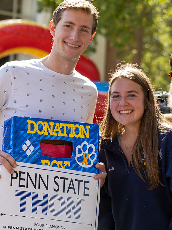 Male and female student hold donation box and sign for Penn State THON.