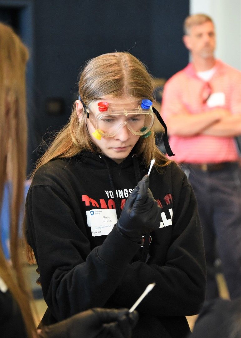 A female student looks closely at a cotton swab while investigating a staged crime scene.