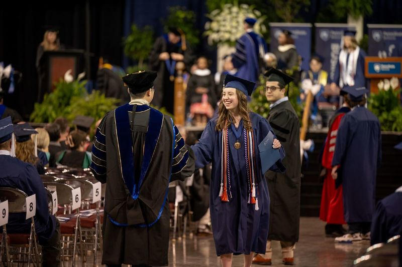 A student shakes the hands of faculty members after receiving her diploma at Penn State Behrend's spring commencement program.