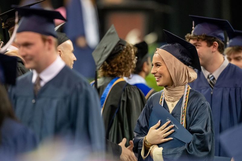 A student in a headscarf holds her diploma at Penn State Behrend's spring commencement program.