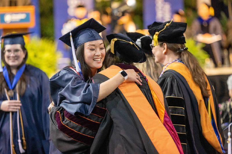 A new Penn State Behrend graduate hugs a faculty member after receiving her diploma.