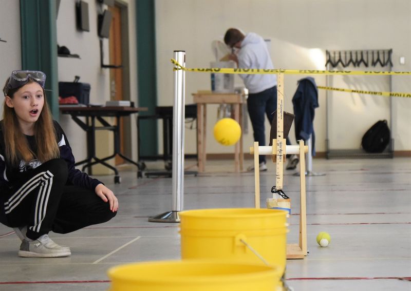 A female student watches a rubber ball fly toward a bucket at the Science Olympiad at Penn State Behrend.