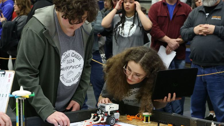 A student and a teacher check a robot on a tabletop obstacle course.