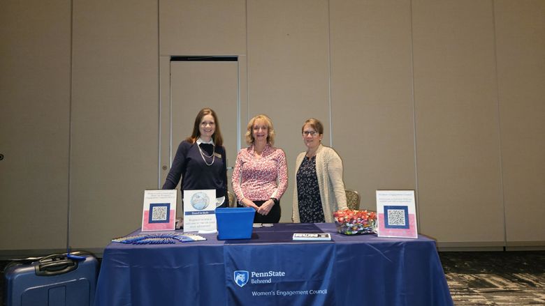 Three women behind a table at a convention