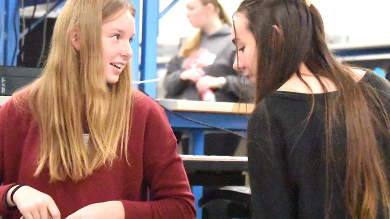 Two high school girls face each other and smile while building a model pipeline out of cardboard tubes.