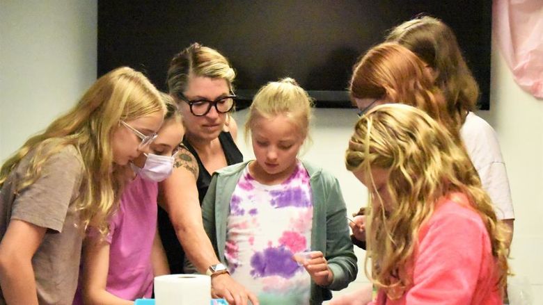 A group of girls gather around a craft table as they make their own lip balms and body sprays.