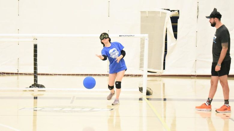 A blind player wearing ski goggles rolls a ball during a game of goalball.