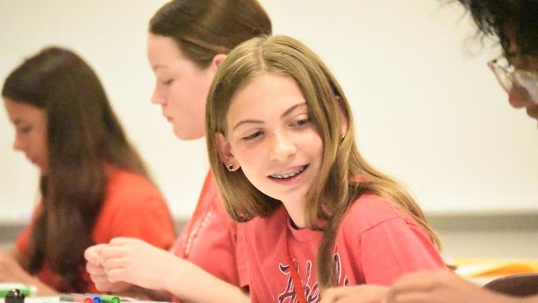 A middle-schooler looks to her side and smiles as a classmate works on a drawing project.