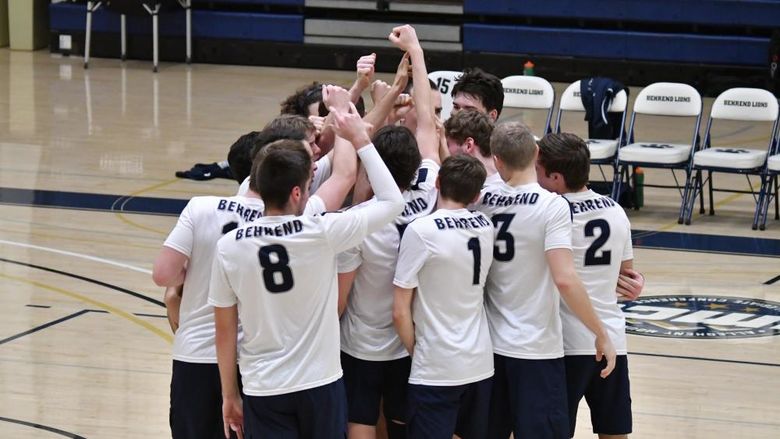 Members of the Penn State Behrend men's volleyball team celebrate in a huddle after winning a point.