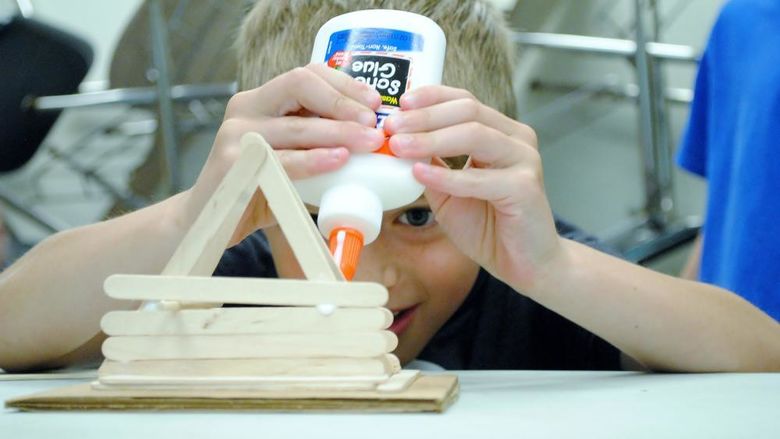 A boy builds a structure with glue and popsicle sticks.