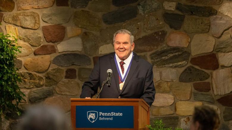 Former Gov. Tom Ridge smiles while standing at a podium at Penn State Behrend.
