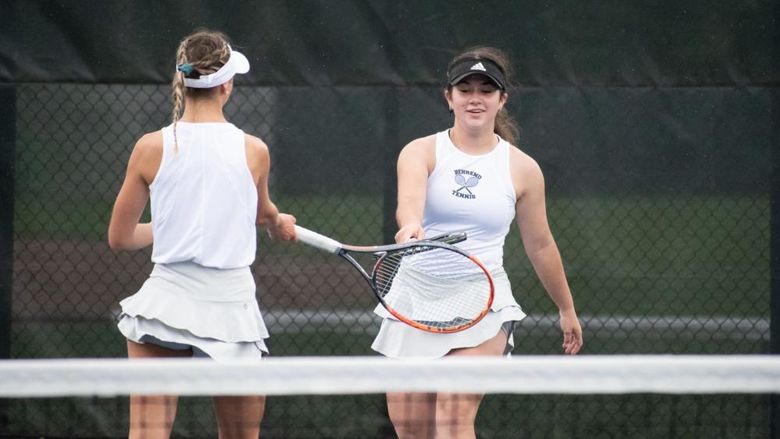 Two Penn State Behrend tennis players touch rackets after scoring a point.