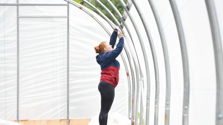 A female student reaches up while installing a section of a high tunnel growing space.