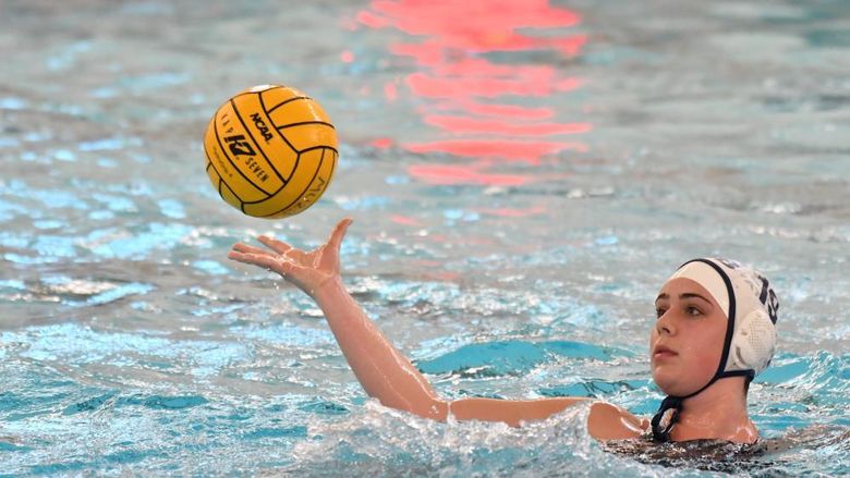 A female water polo player catches the ball while treading water.