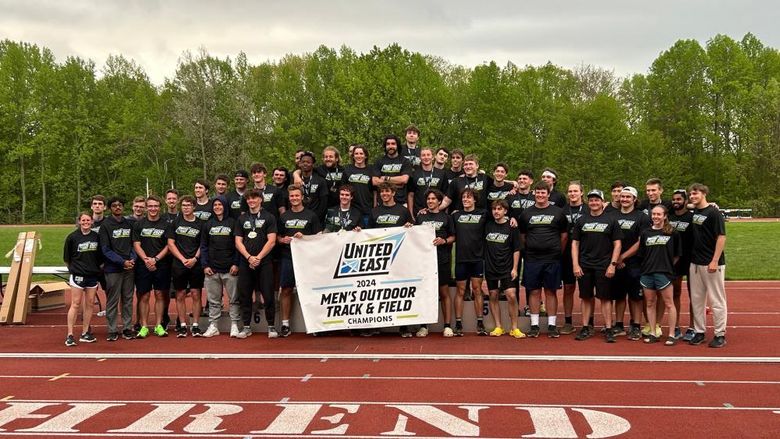 The Penn State Behrend men's track and field team celebrates with the United East championship banner.