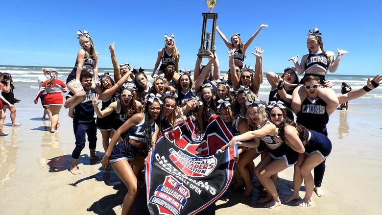 The Penn State Behrend cheer team holds the trophy on the beach in Florida.