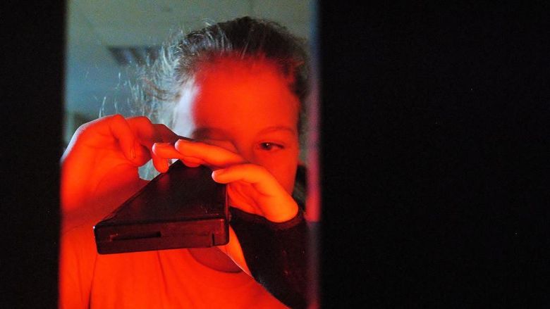 A girl looks through a light spectrum during a science experiment.