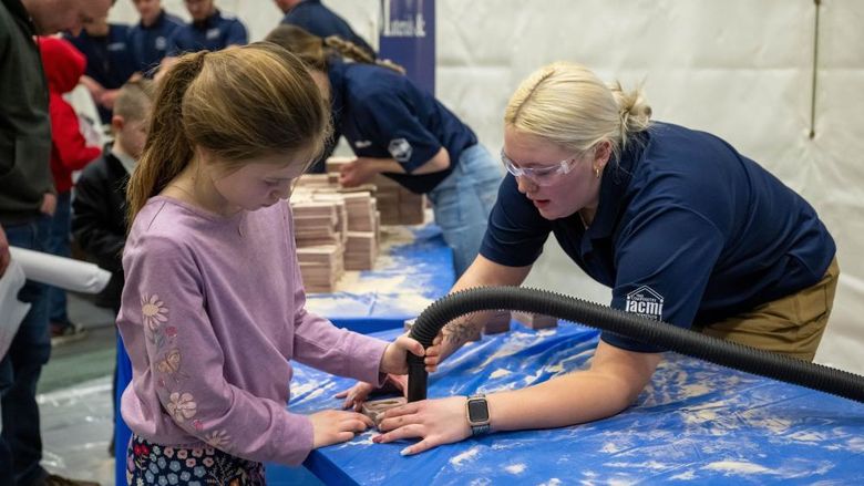 A volunteer helps a child clean out a sand mold used in metal-casting.