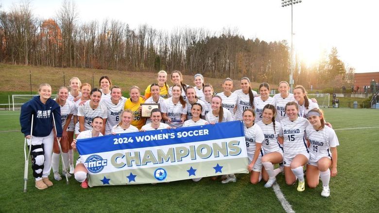 The Penn State Behrend women's soccer team poses with the AMCC championship banner.