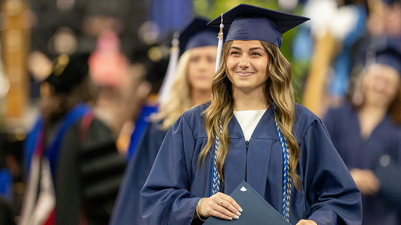Young woman in a graduation cap and gown holding a diploma at a ceremony.