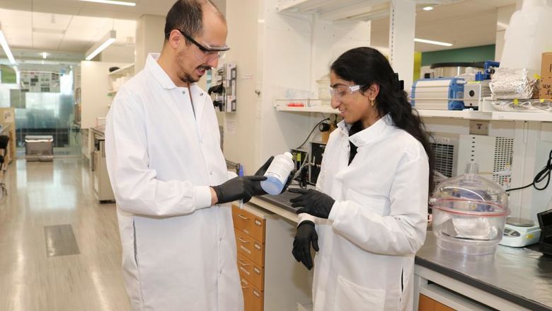 Two people in lab coats check a bottle of chemicals