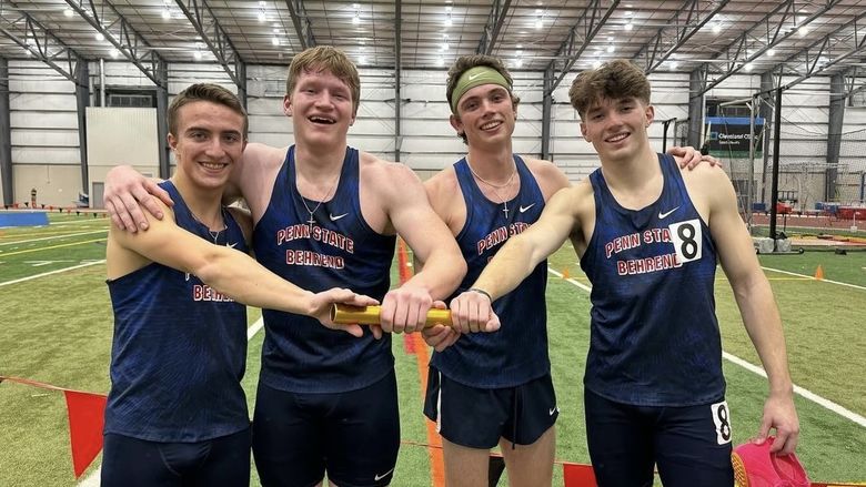 Four Penn State Behrend runners pose while holding a track baton.