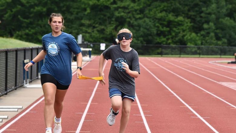 A vision-impaired athlete runs with a guide while holding a tether.