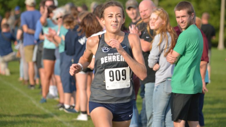 A female Penn State Behrend runner competes in a cross country race.