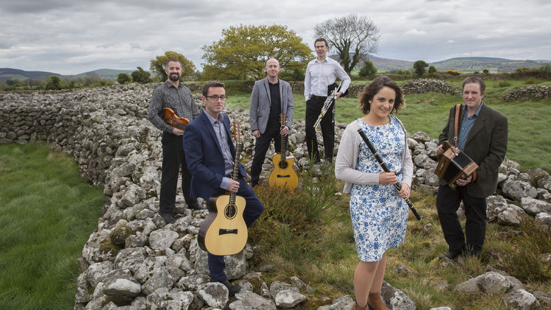 The musicians in the band Danu pose on rocks in a country field.