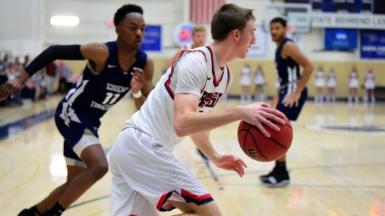 A Penn State Behrend basketball player dribbles toward the net.