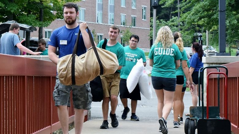 Student volunteers carry items into a Penn State Behrend residence hall.