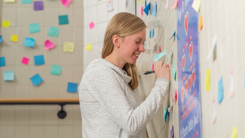 Penn State Behrend alumna Ashlyn Kelly writes a positive message on a sticky note in the Random Acts of Kindness stairwell at Penn State Behrend.