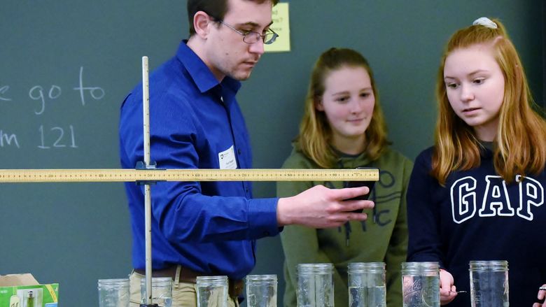 An instructor measures the pitch of a water glass struck by two students in a regional Science Olympiad event.