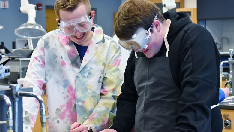 Two students wearing safety goggles conduct a chemistry experiment at Penn State Behrend