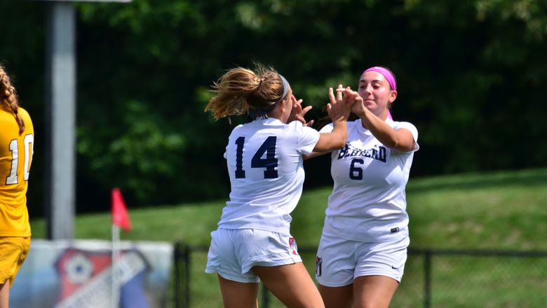 Two Penn State Behrend soccer players celebrate after scoring a goal.