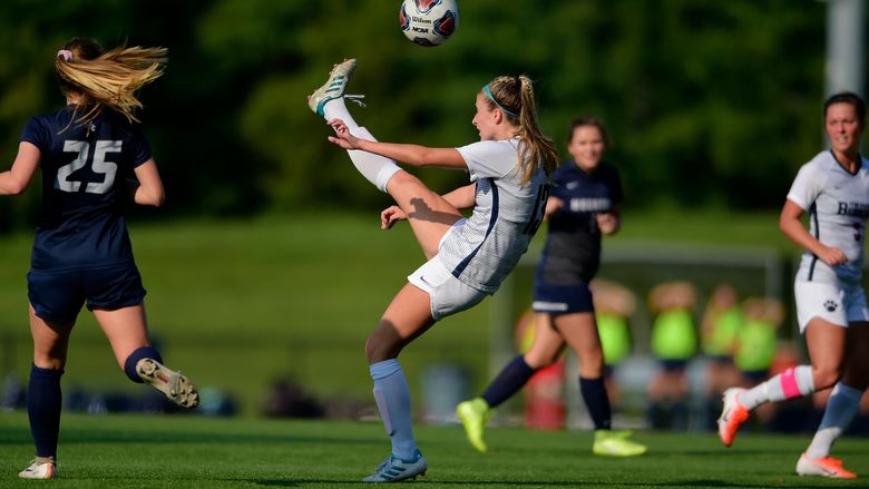 A Penn State Behrend soccer player kicks the ball above her head.