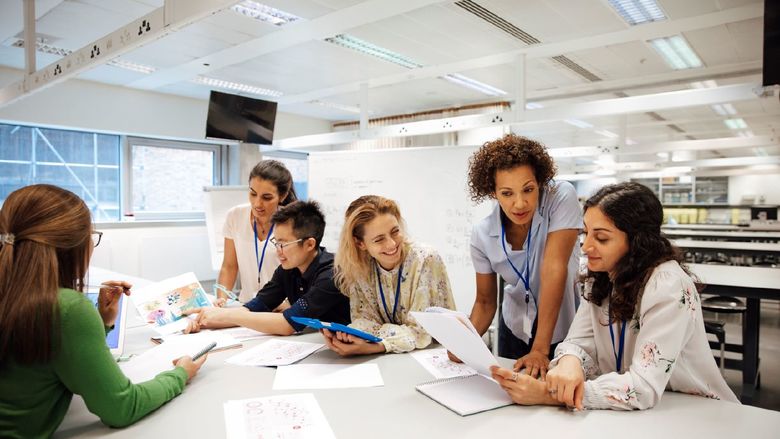Adult students are gathered at a table working on an academic project together.