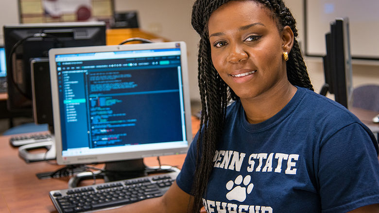 A student poses in front of a computer in a Penn State Behrend computer lab.