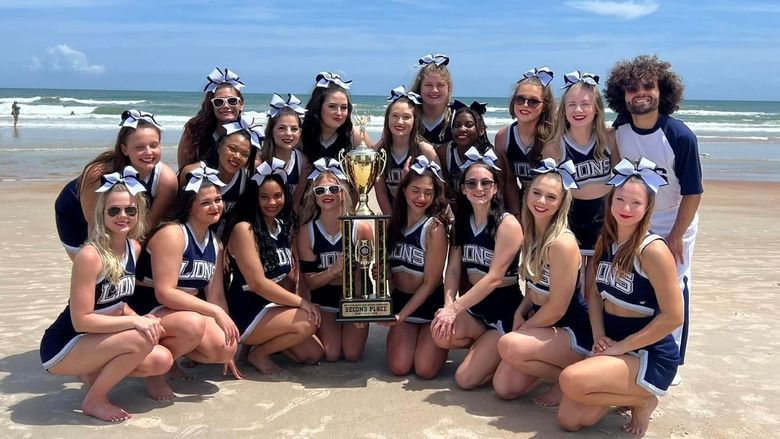 Penn State Behrend's competitive cheerleading team poses with a trophy on the beach in Florida.